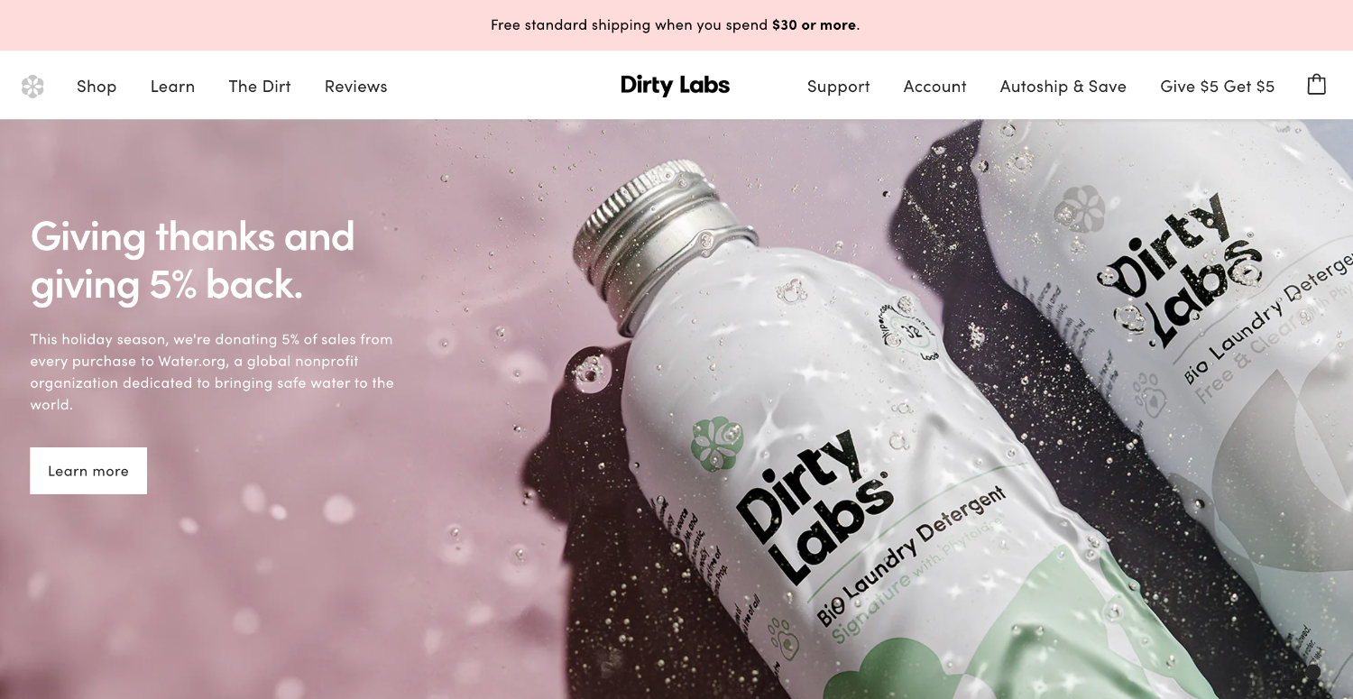 Two Dirty Labs bio laundry detergent bottles in water with bubbles, promoting a donation campaign.